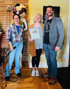 Historic Preservation Commission Chair Christen DePetro stands next to Kelly Langley Cook and Jeff Cook. Kelly holds up the award for rehabilitating the Ambry.