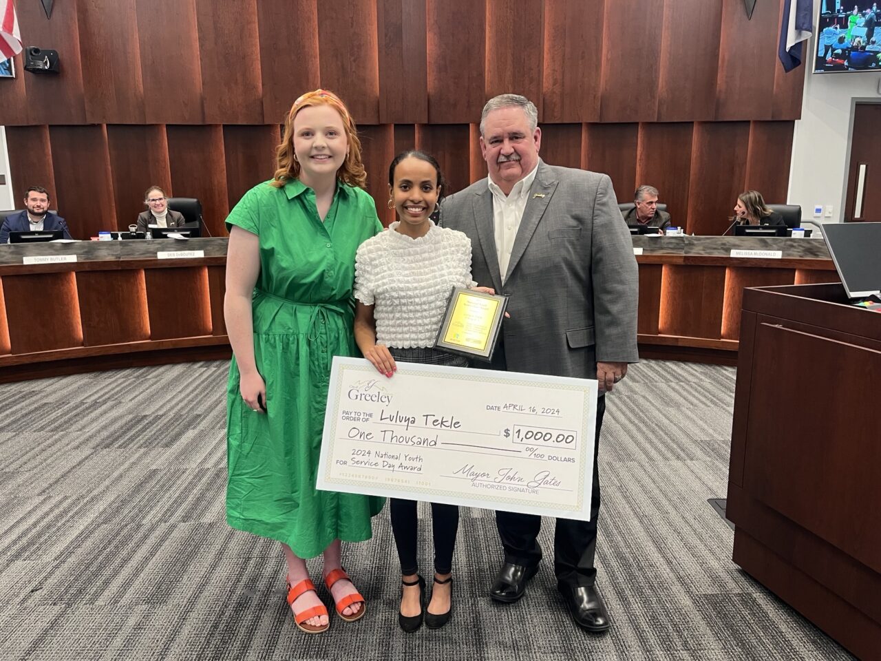 Greeley Mayor John Gates presenting an oversized check in city council chambers to a female high school student who won the 2024 National Youth Service Day Awards $1,000 scholarship.