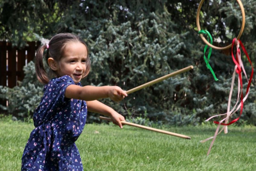 A child uses sticks to toss a wooden hoop.