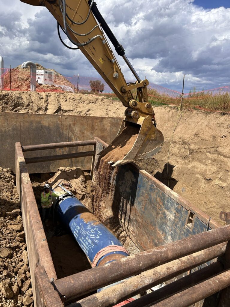 A worker oversees dirt being dropped on a pipeline as it is buried.