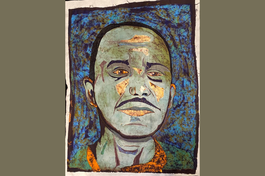 Fabric and embroidery creates a portrait of a man with short hair and a mustache in shades of blues, greens, gold, black and orange.