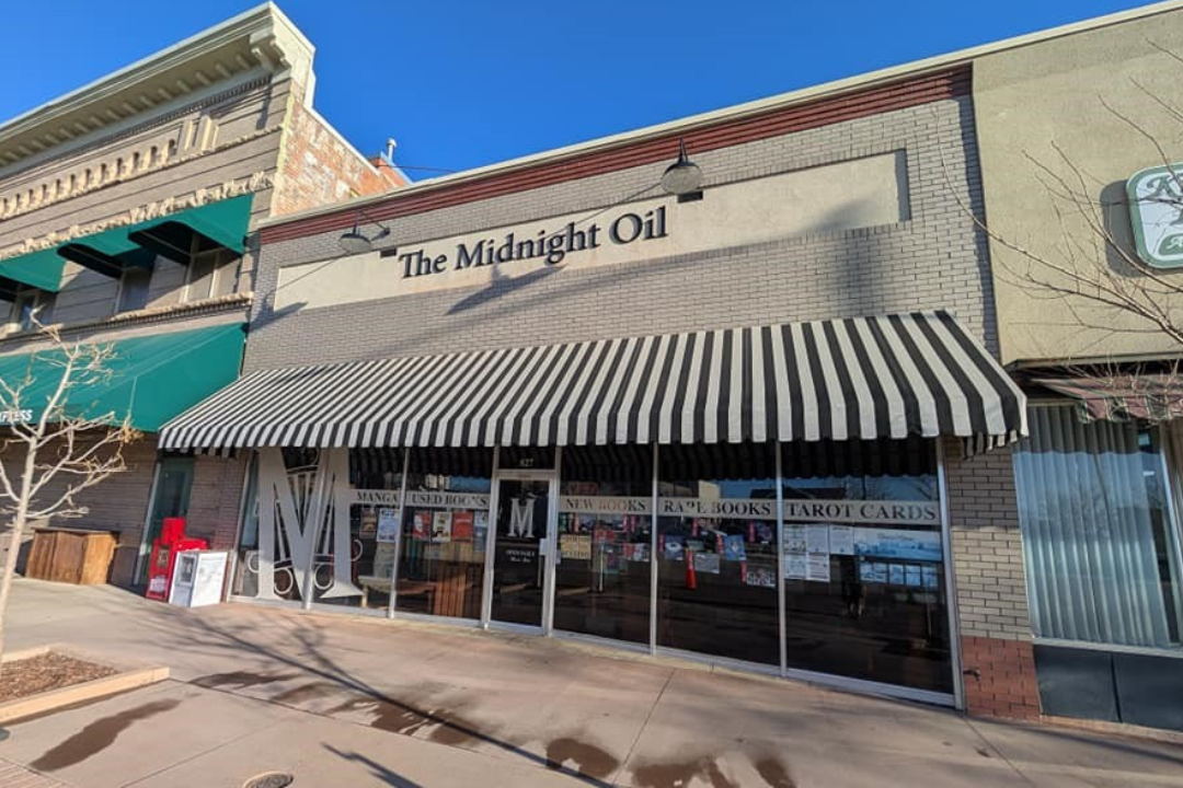 Front entrance of The Midnight Oil Bookstore with a large striped awning on a brick exterior.