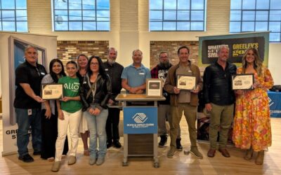 Group of eleven people stand in a row holding award plaques. There is a podium in the middle of the group that says Boys and Girl Club of Weld County.