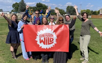 A group of people smile while holding a red banner reading “Generation Wild" with a park and green open space in the background.