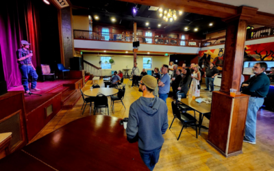 A person speaks on stage with a microphone at the gBETA Greeley Fall 2025 Kickoff Party while attendees watch from tables and the balcony.