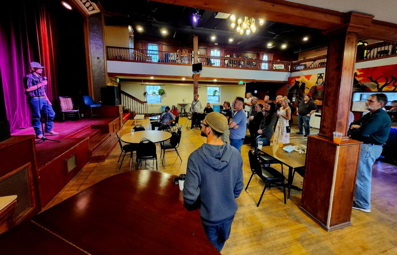A person speaks on stage with a microphone at the gBETA Greeley Fall 2025 Kickoff Party while attendees watch from tables and the balcony.
