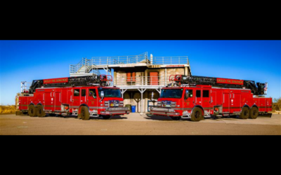 Two red firetrucks park near a training structure.