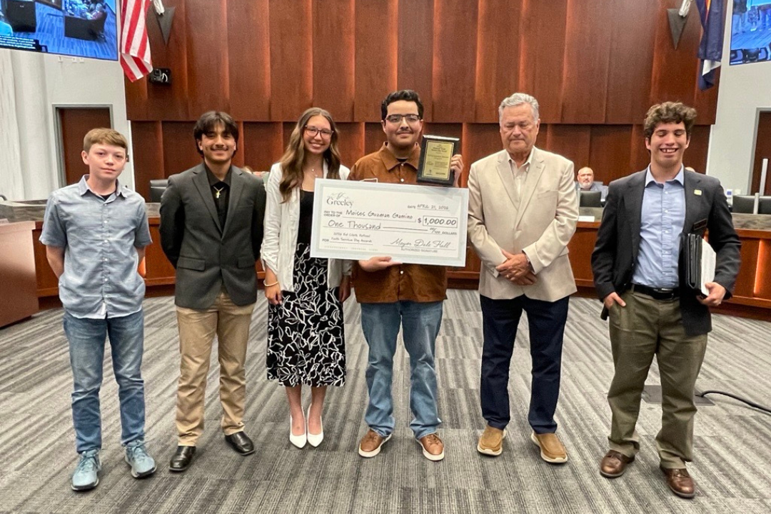 Mayor presents oversized $1,000 scholarship check at a city council meeting to a young man, a Greeley high school senior who won the 2026 Ed Clark National Youth Service Day Award. 