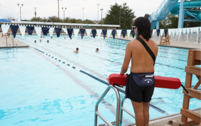 Lifeguard watches over swimmers in the outdoor pool on a summer day.